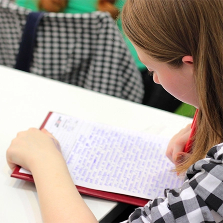 A photograph taken over a student's shoulder of them writing on a piece of lined paper